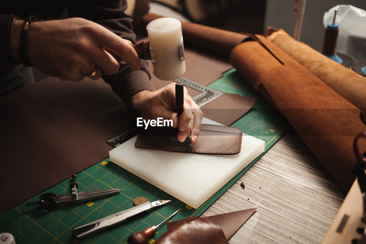 Leatherworker beats with hammer. tanner works with leather, small business, production.