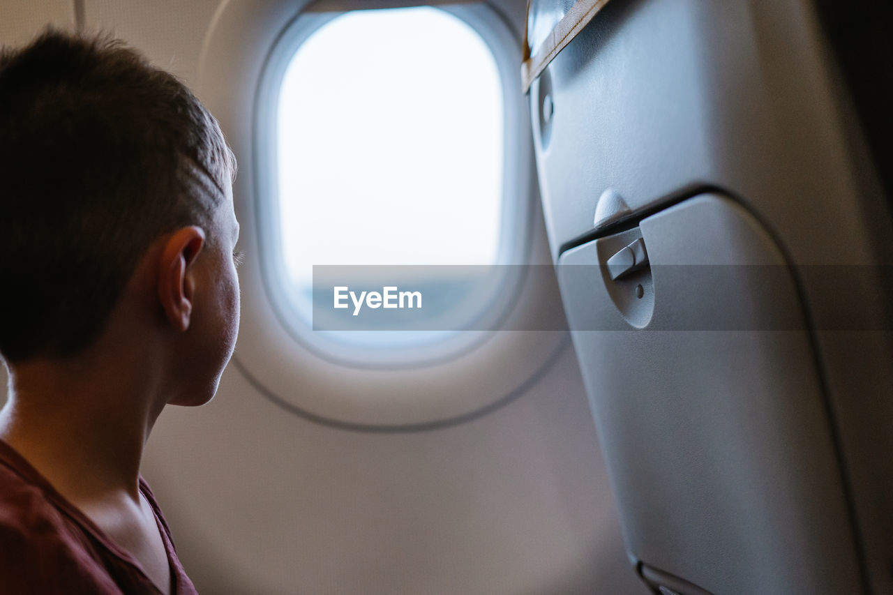 Side view of calm boy sitting on chair looking out the windows in plane