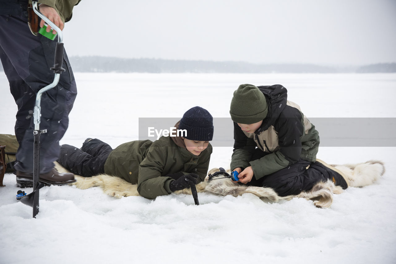 Boys in warm clothing ice fishing at frozen lake during vacation
