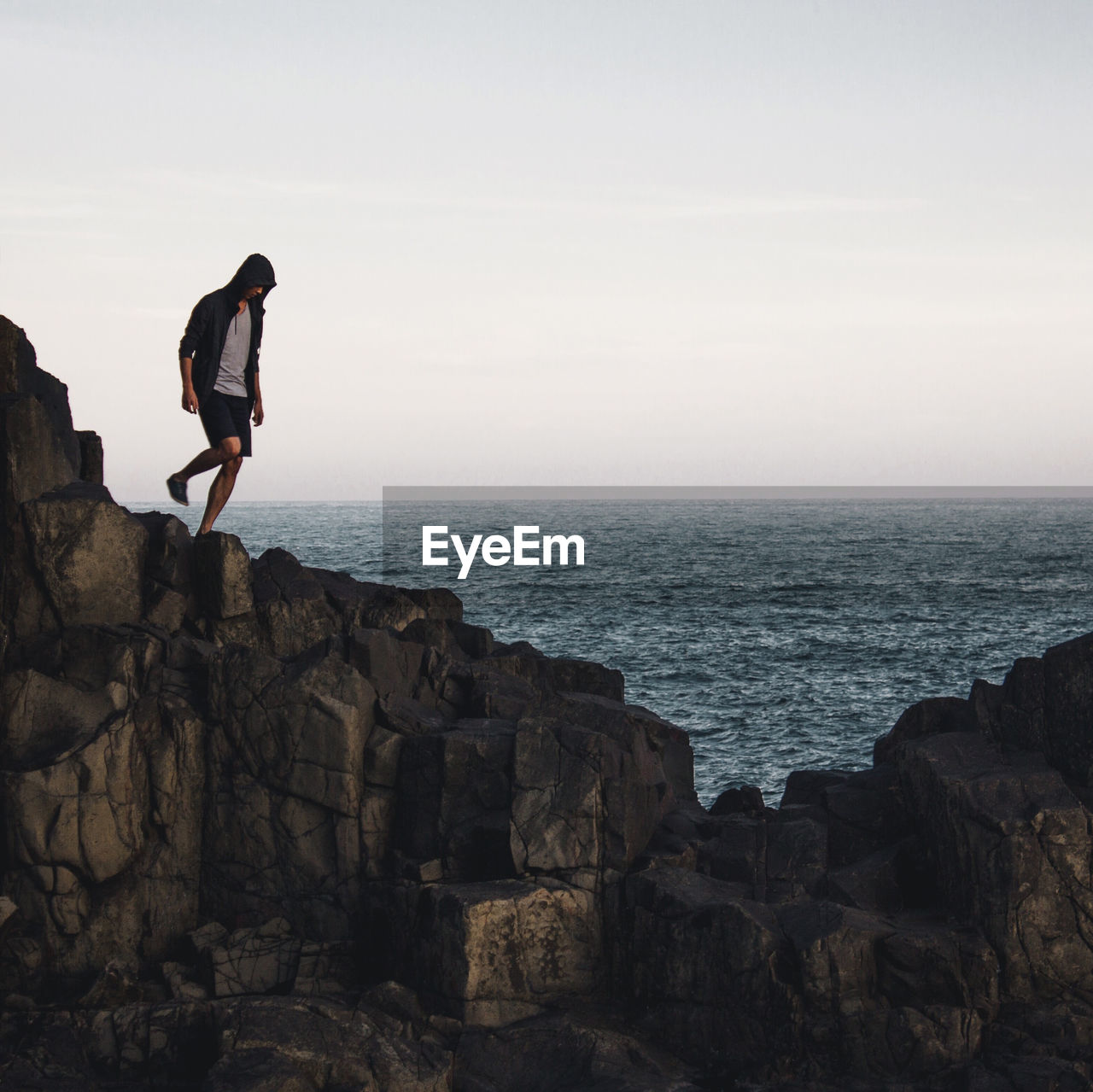 Man standing on cliff by sea against sky