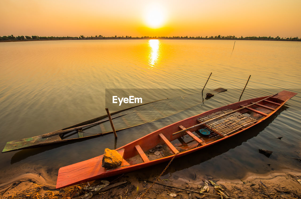 Boat moored in lake against sky during sunset