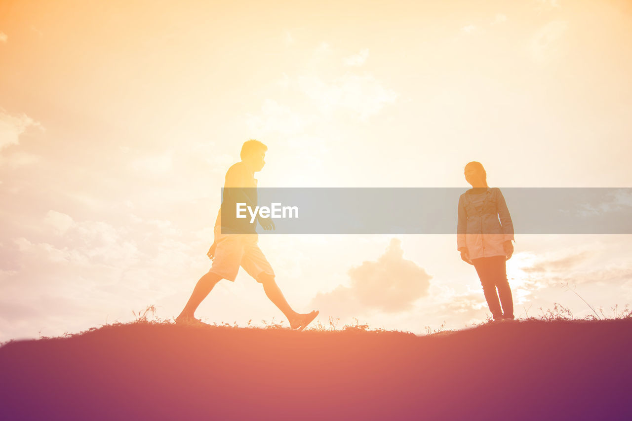 LOW SECTION OF SILHOUETTE WOMAN WALKING ON FIELD AGAINST SKY