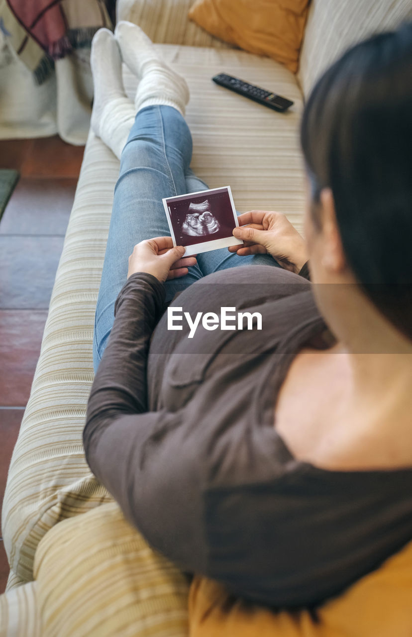 High angle view of woman holding ultrasound while sitting on sofa at home