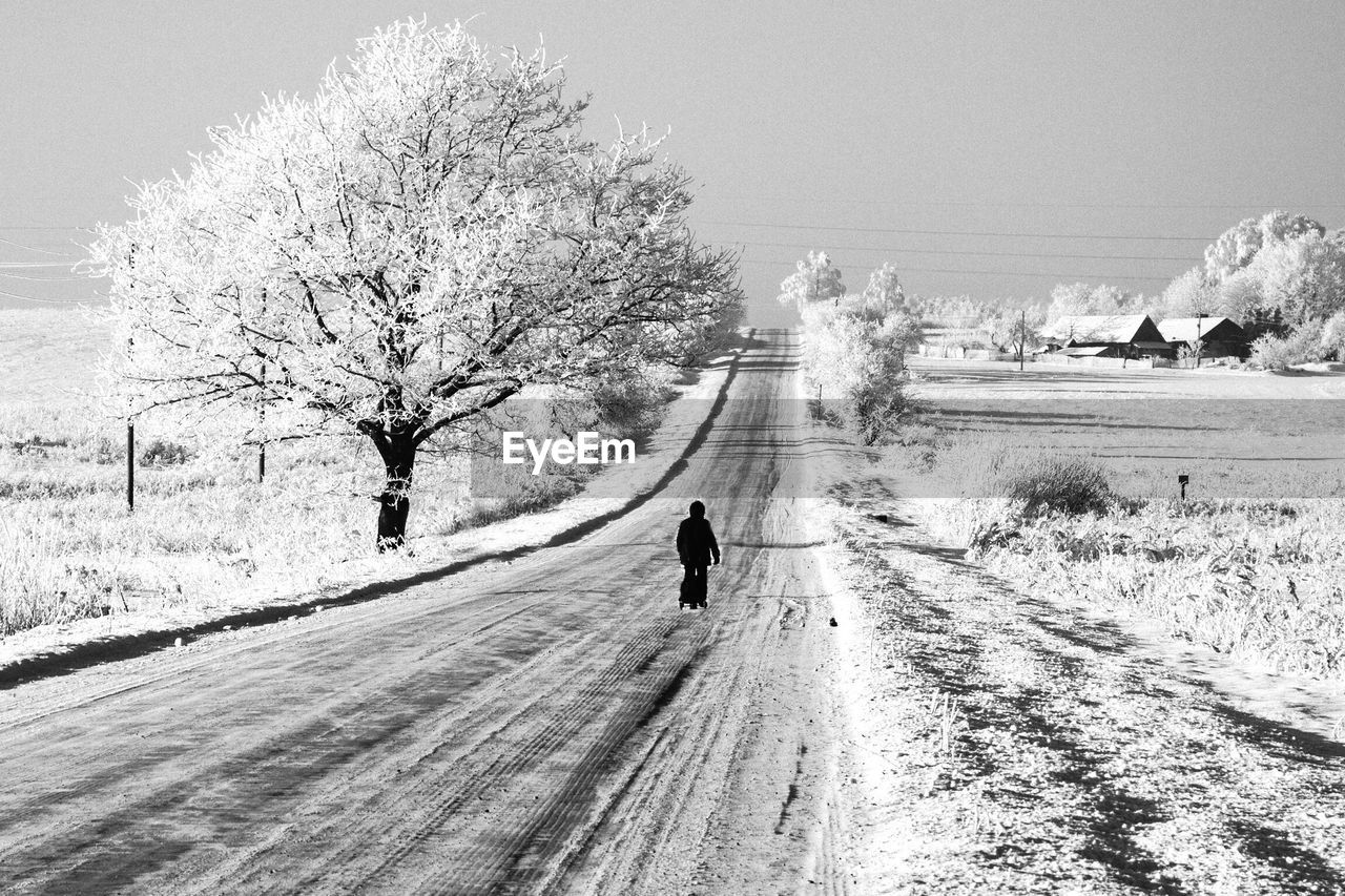 Rear view of person walking on snow covered road and landscape