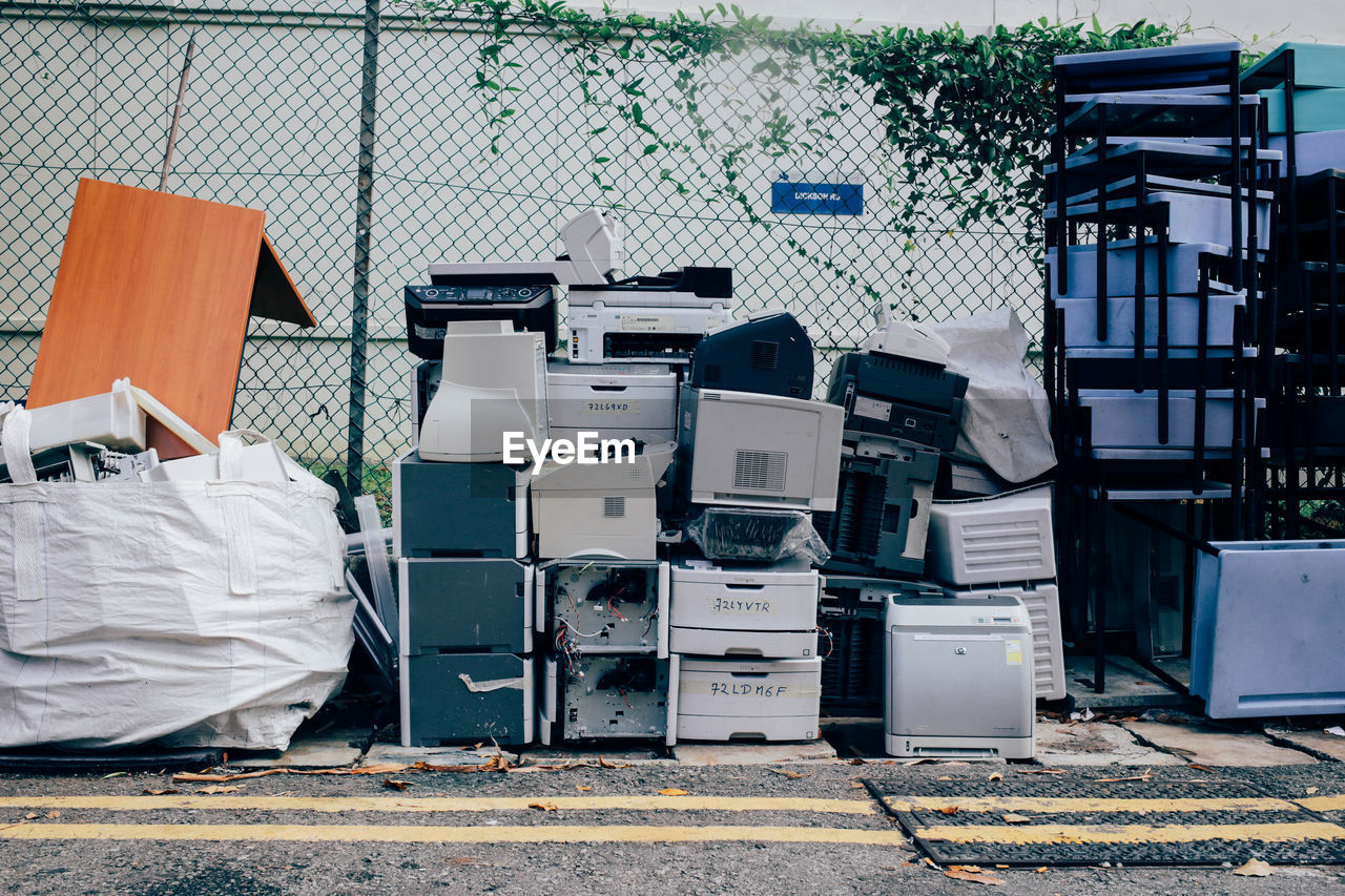 Abandoned stacked computer printers against fence