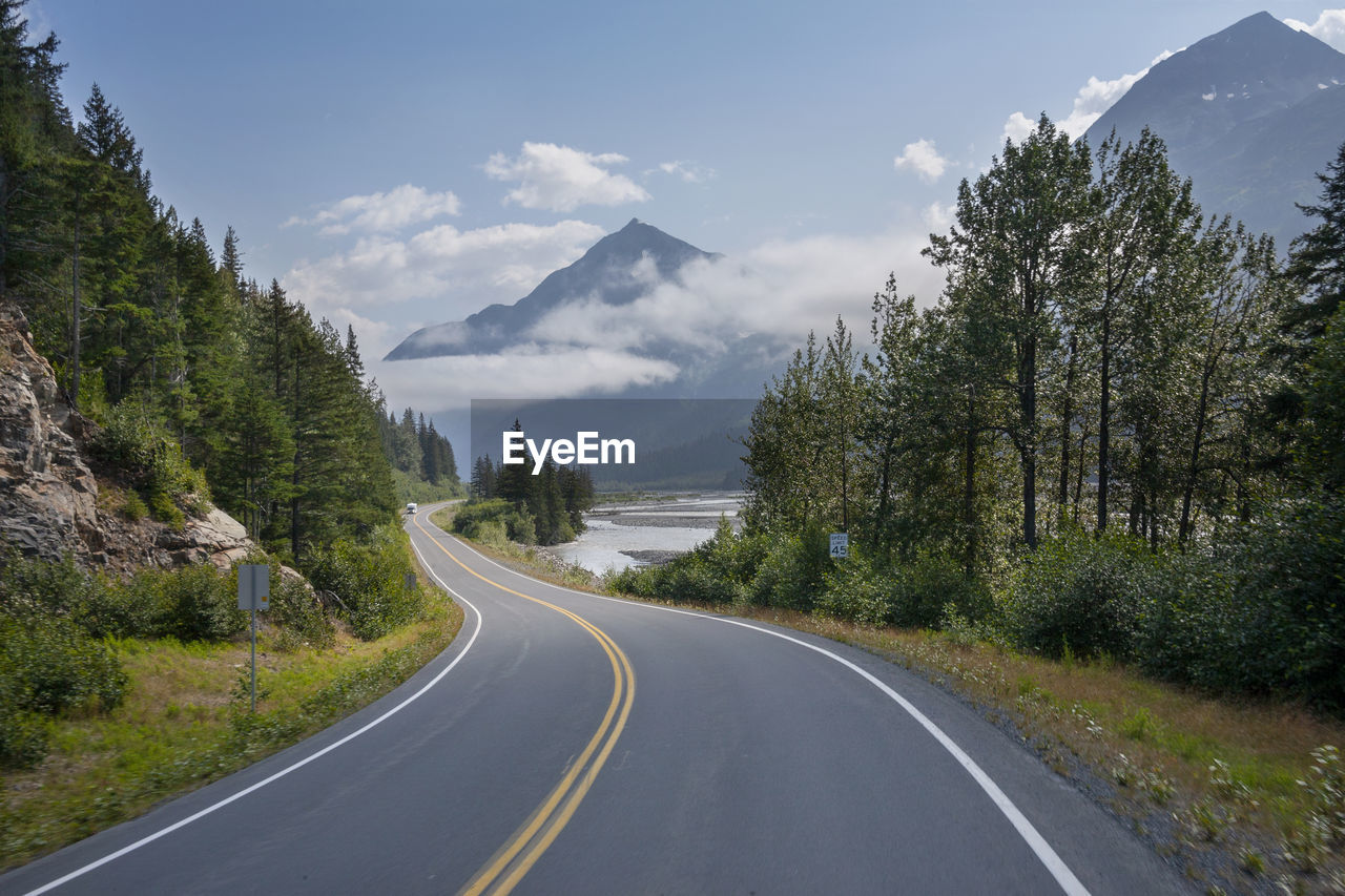 road amidst trees and mountains against sky