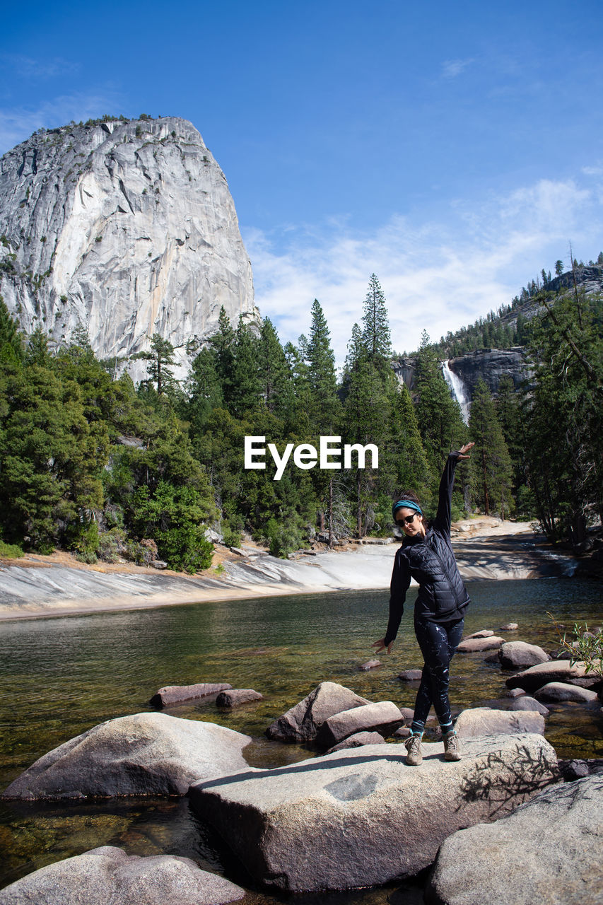 Full length of woman standing on rock at river against sky