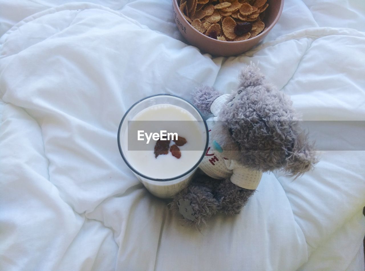 High angle view of teddy bear with milk glass and breakfast cereal on bed