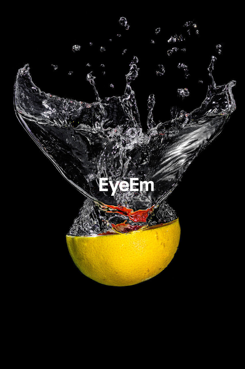 Close-up of lemon splashing in water against black background