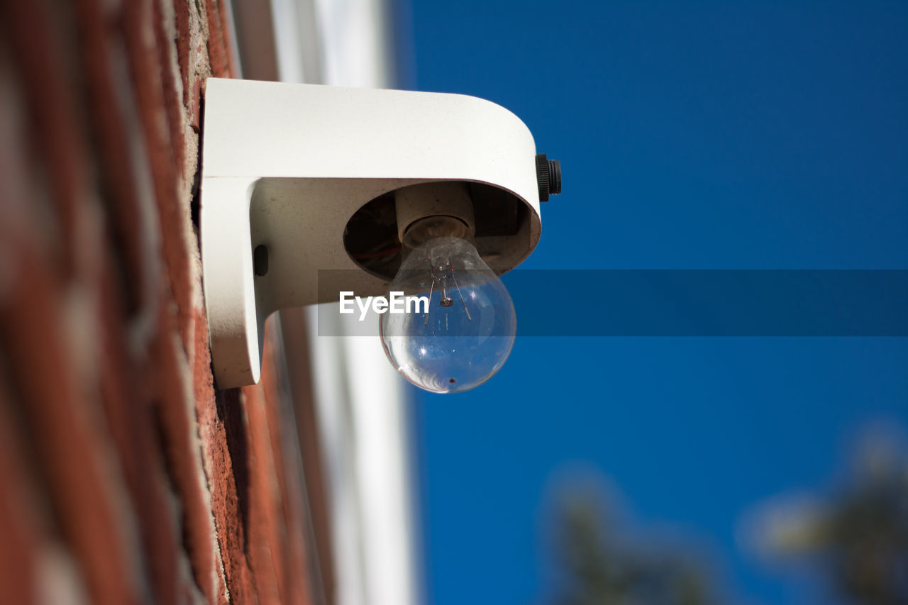 Low angle view of light bulb mounted on brick wall against clear blue sky