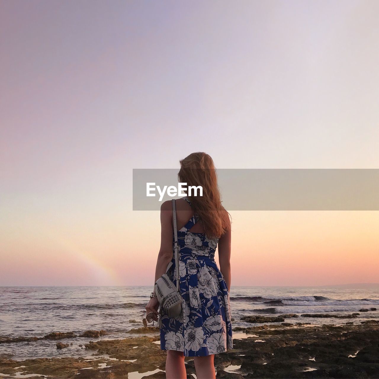 Rear view of woman standing at beach against sky during sunset