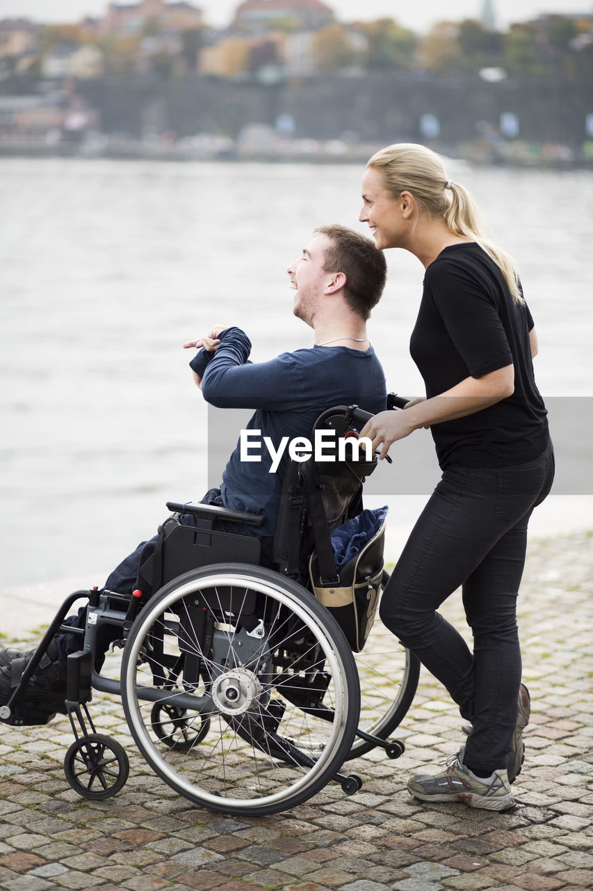 Happy disabled man with caretaker enjoying view by lake