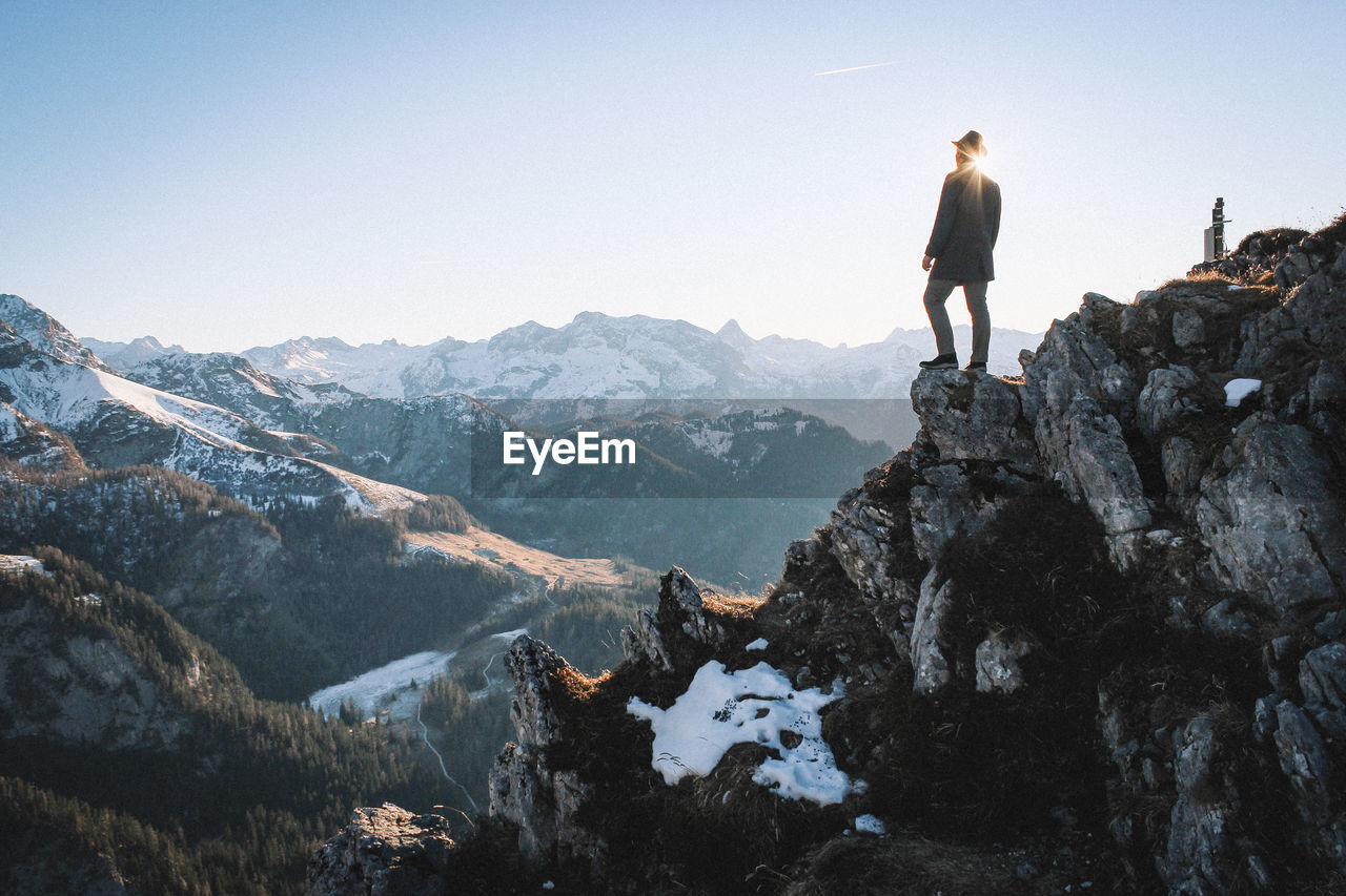 Low angle view of man standing on rocky mountains against clear sky during sunny day