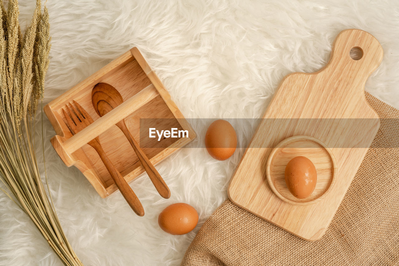 High angle view of egg and wheat with wooden eating utensils on table