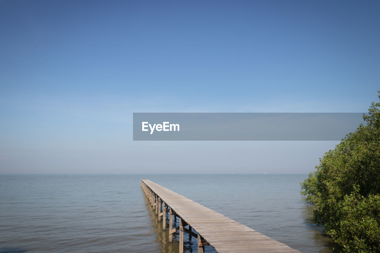 Pier over sea against clear blue sky