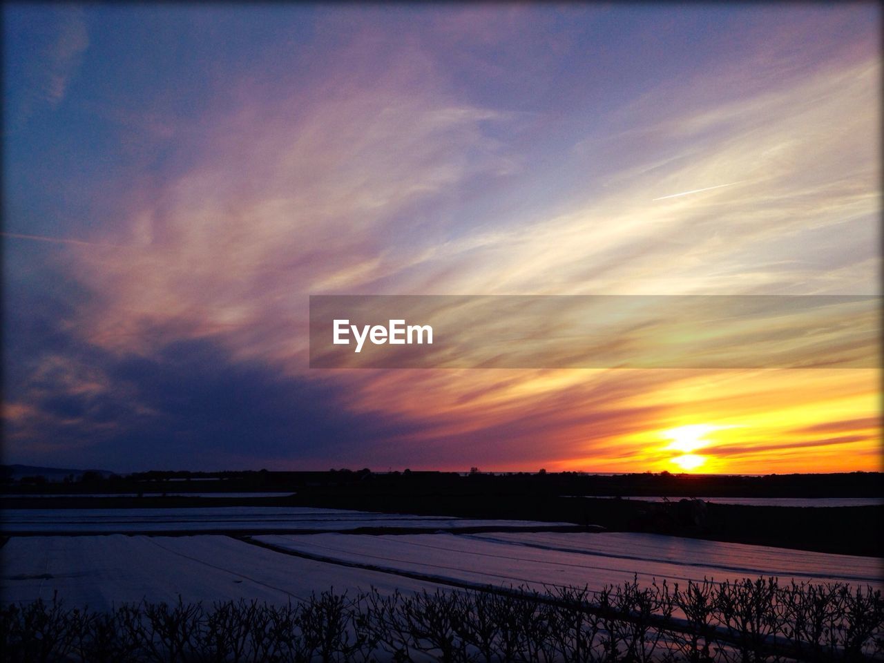 Snow covered farm against sky during sunset