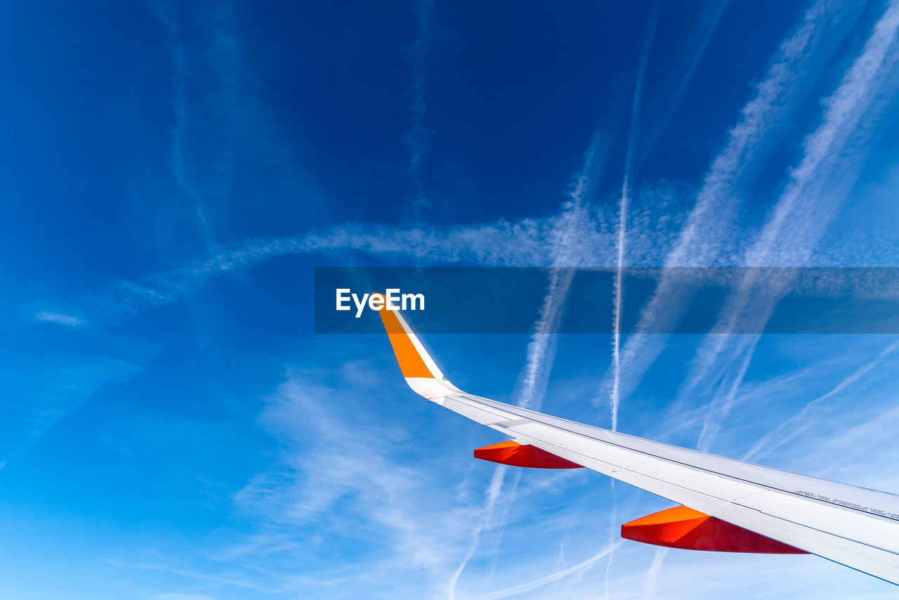 Wing of airplane flying against blue sky with contrails. traveling concept