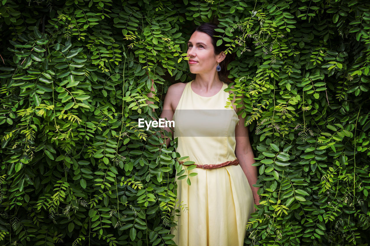 Woman staying surrounded by lush green plants, touching leaves.