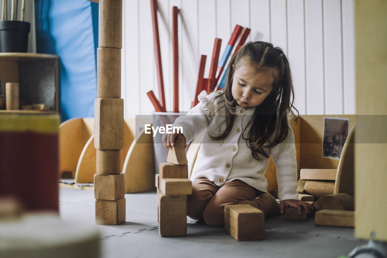 Girl stacking toy blocks while sitting in kindergarten