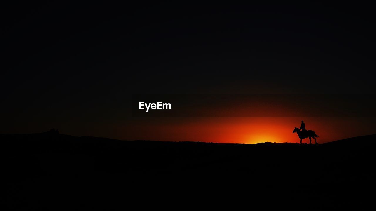 Silhouette man on horseback on landscape at sunset