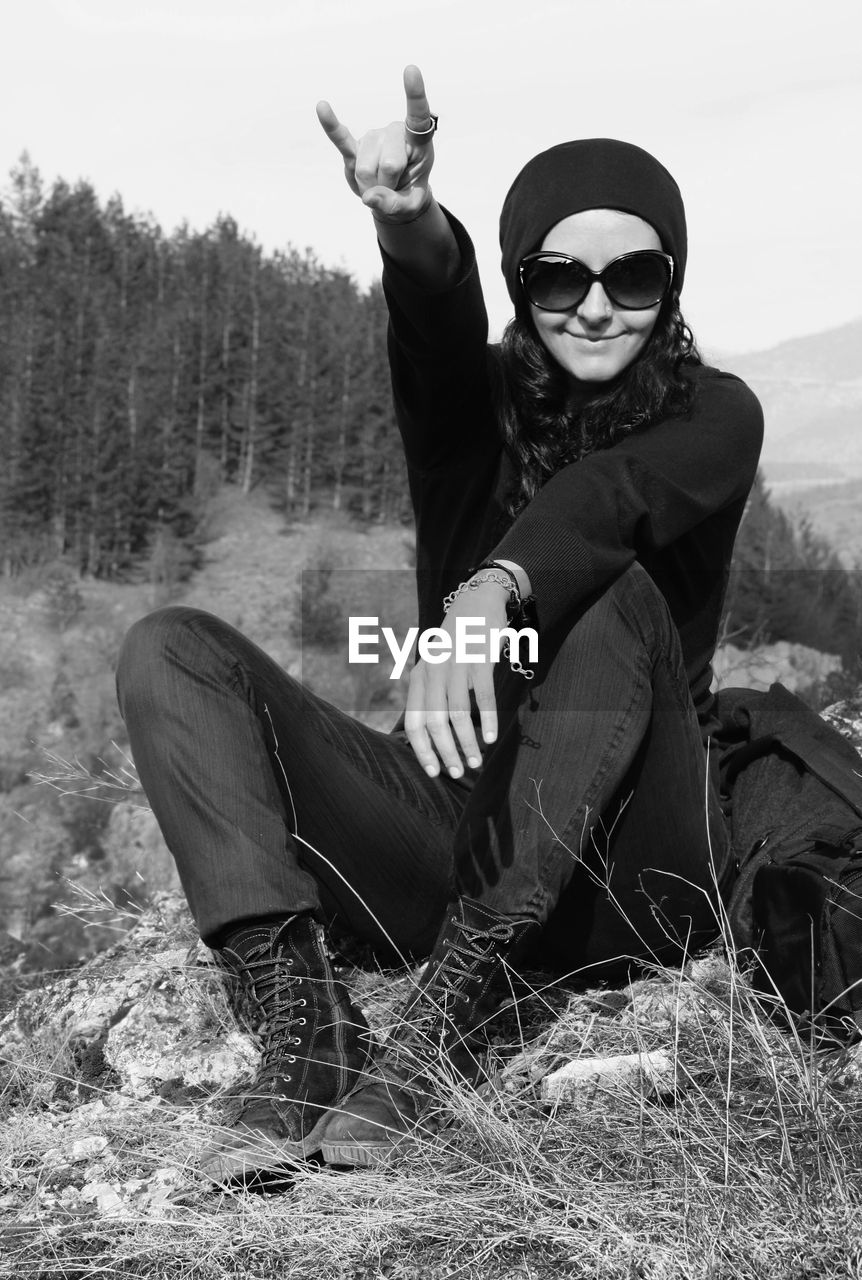 Portrait of smiling woman gesturing horn sign on field