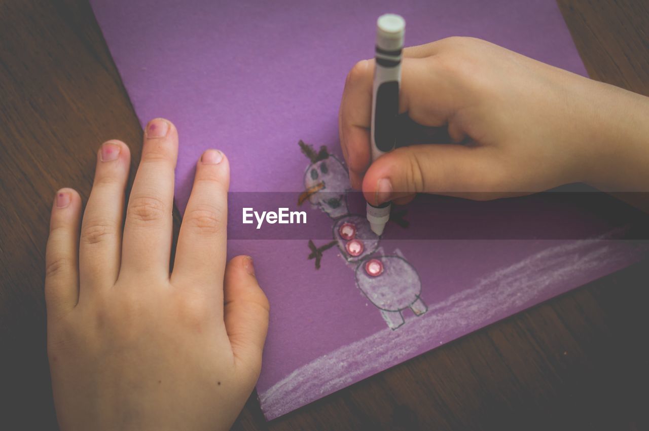 Cropped image of hands drawing on purple paper