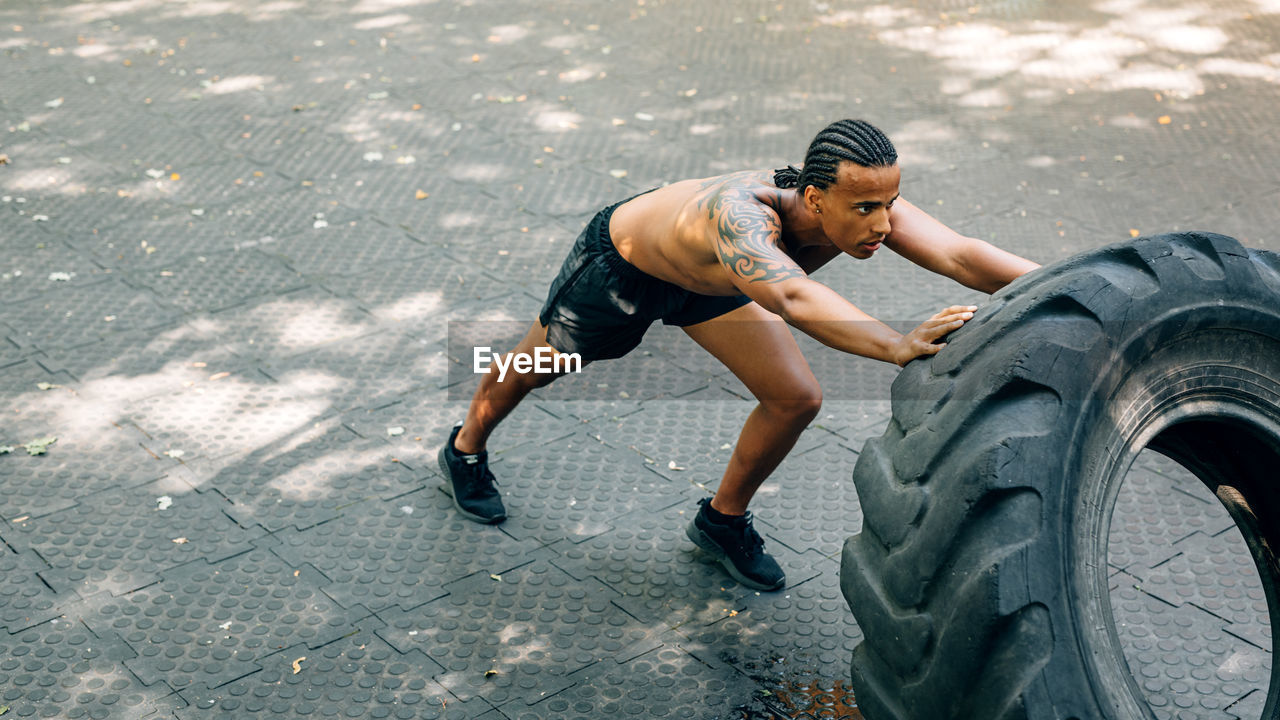 Full length of man lifting up tire on footpath