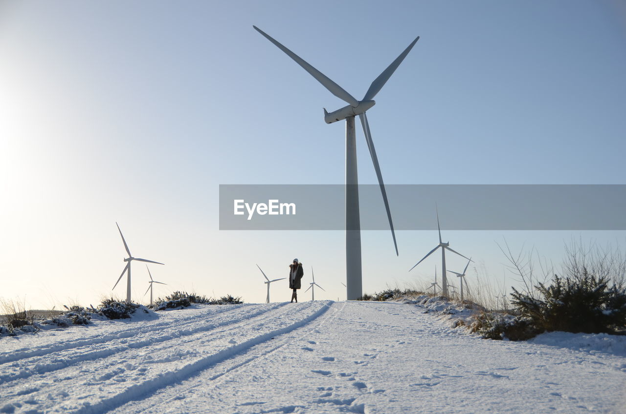 Wind turbines on snowed landscape against clear sky