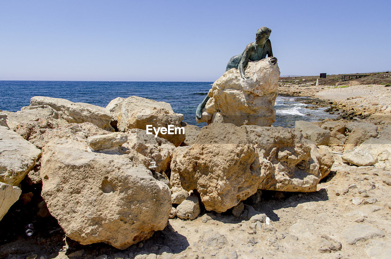 rock, sea, sky, land, water, beach, nature, clear sky, scenics - nature, shore, coast, geology, sand, beauty in nature, horizon, horizon over water, tranquility, sunny, landscape, day, no people, travel destinations, ocean, terrain, sunlight, blue, tranquil scene, travel, cliff, outdoors, environment, rock formation