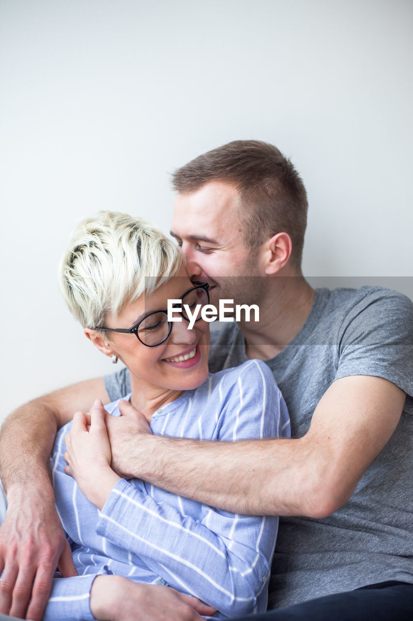 Happy couple sitting by wall at home