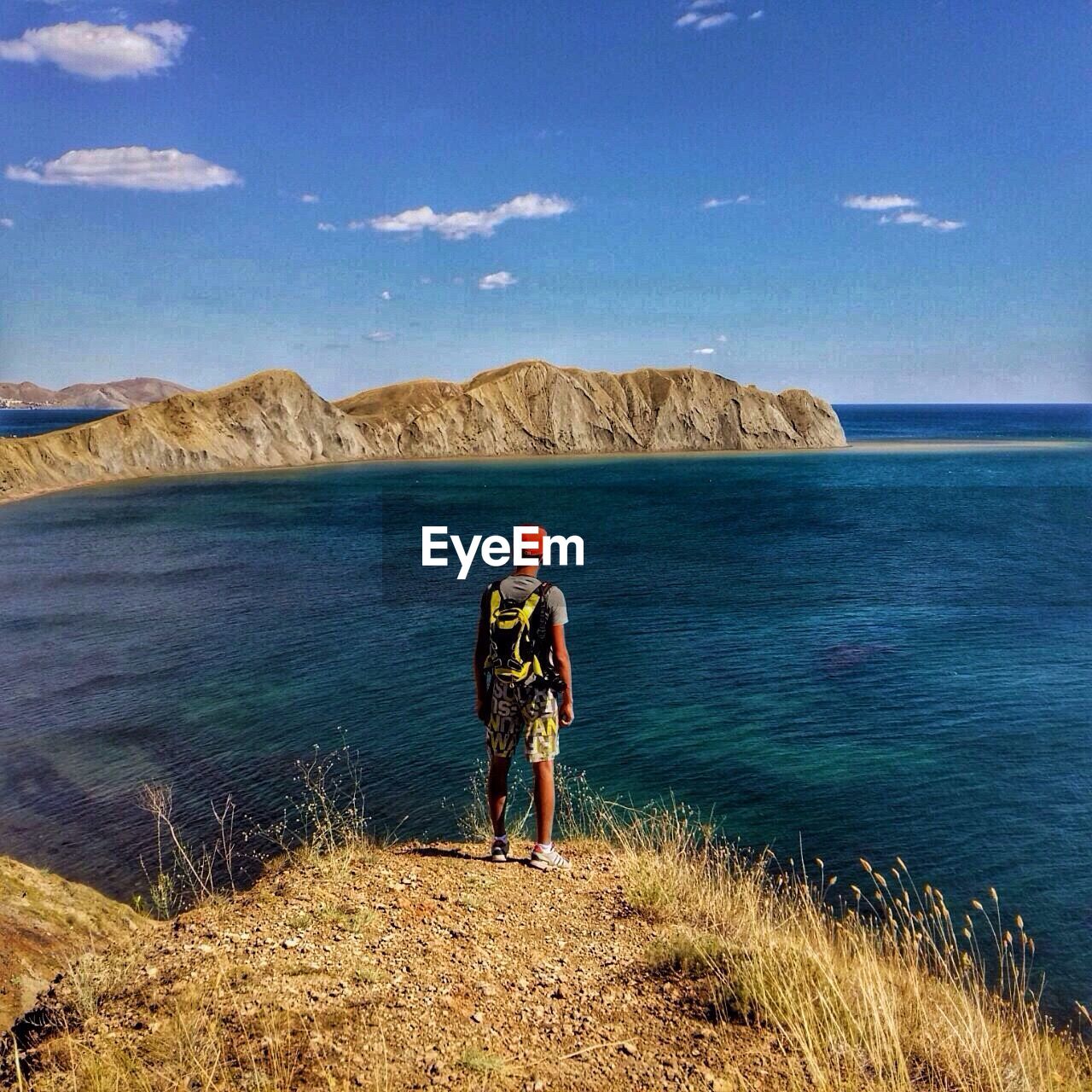 Rear view of man standing on cliff by sea against sky