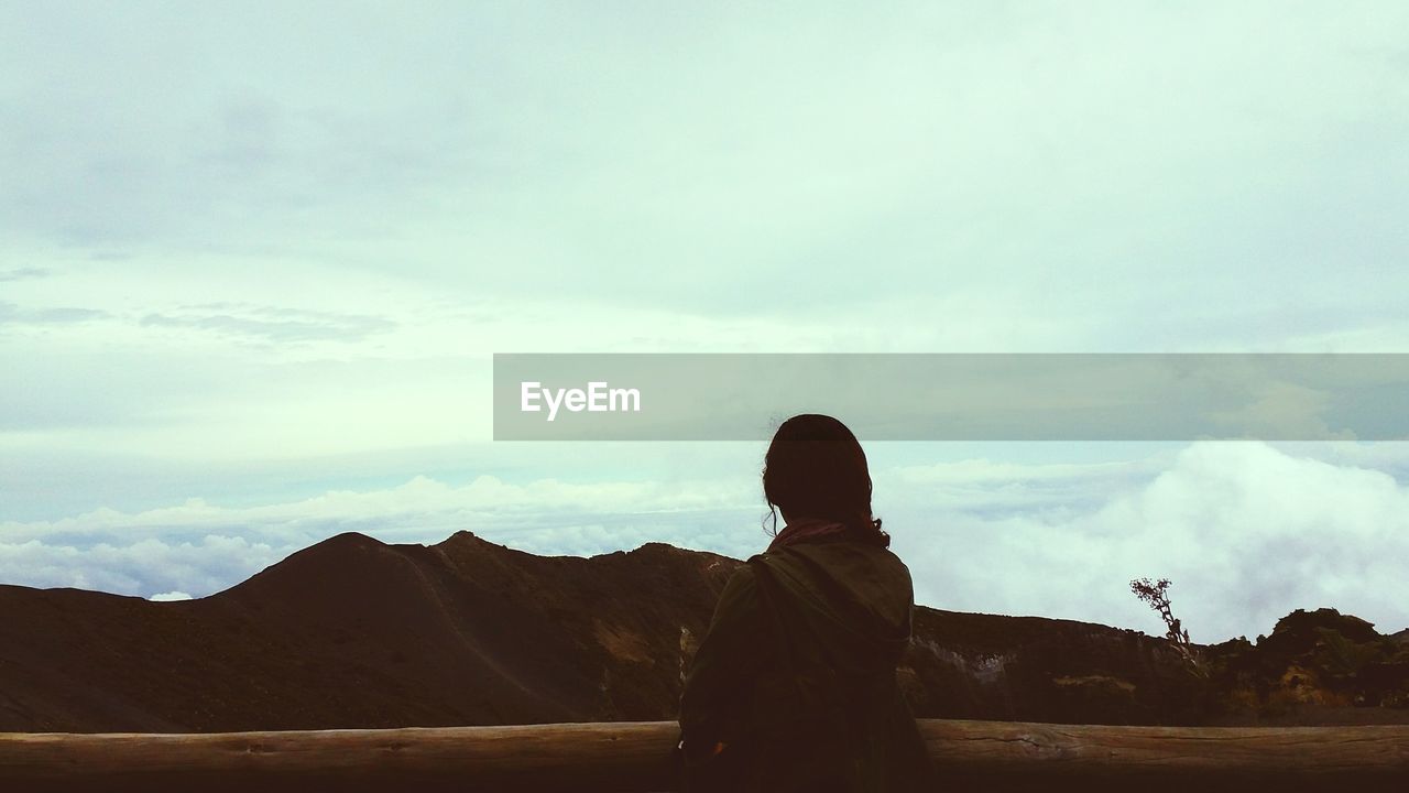 Rear view of woman standing against mountains and cloudy sky