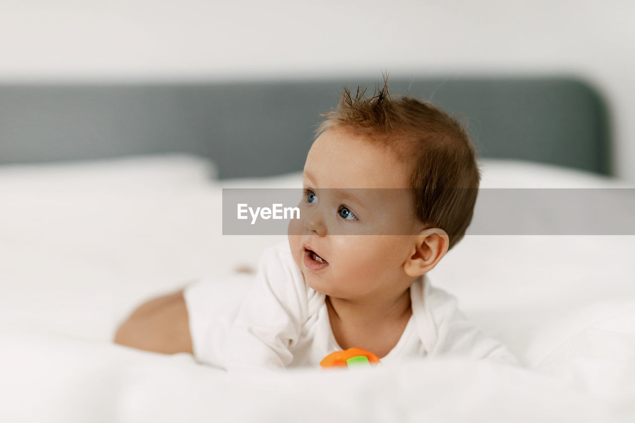 Cute baby looking away while lying down on bed