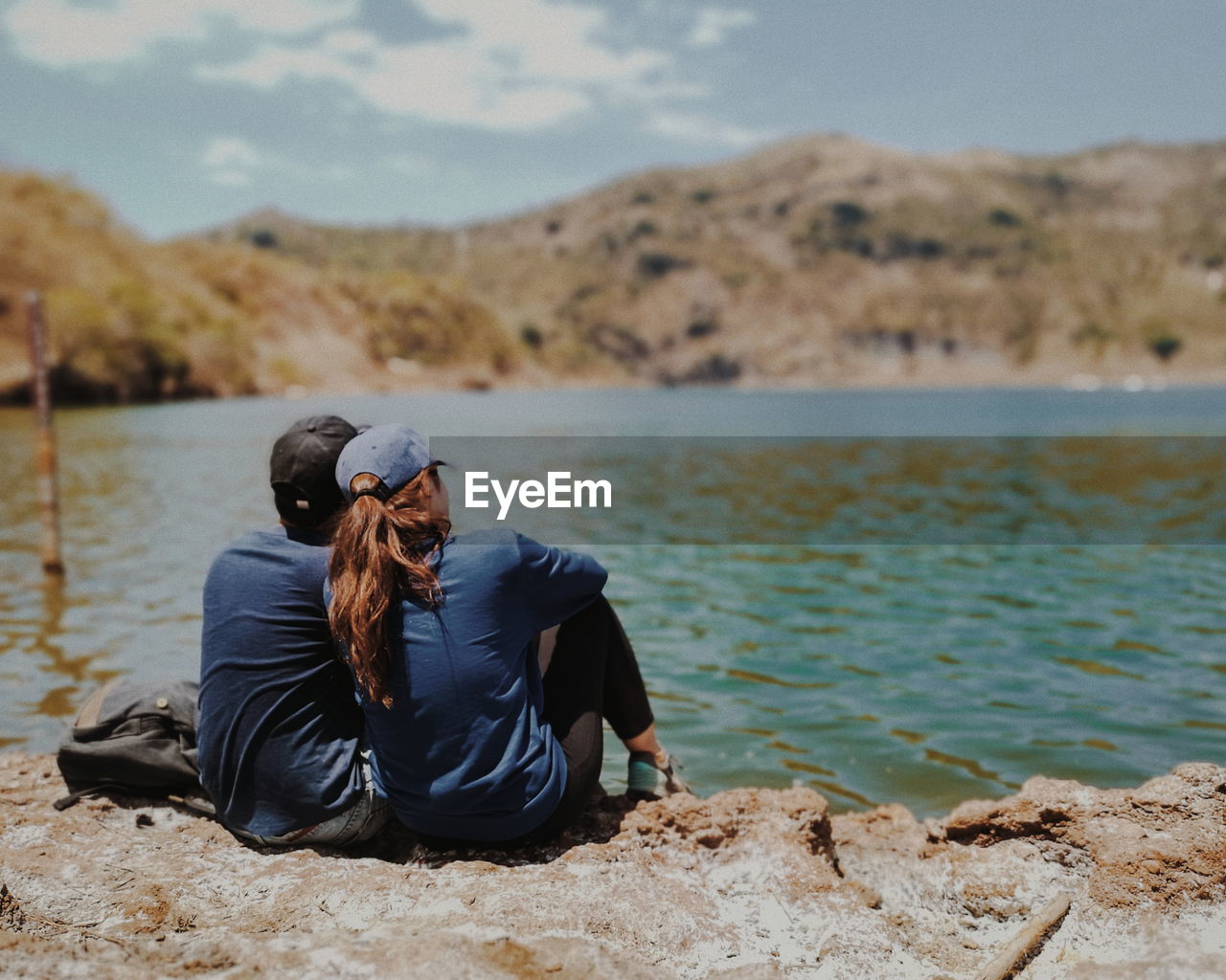 Rear view of couple sitting on rock at beach against sky