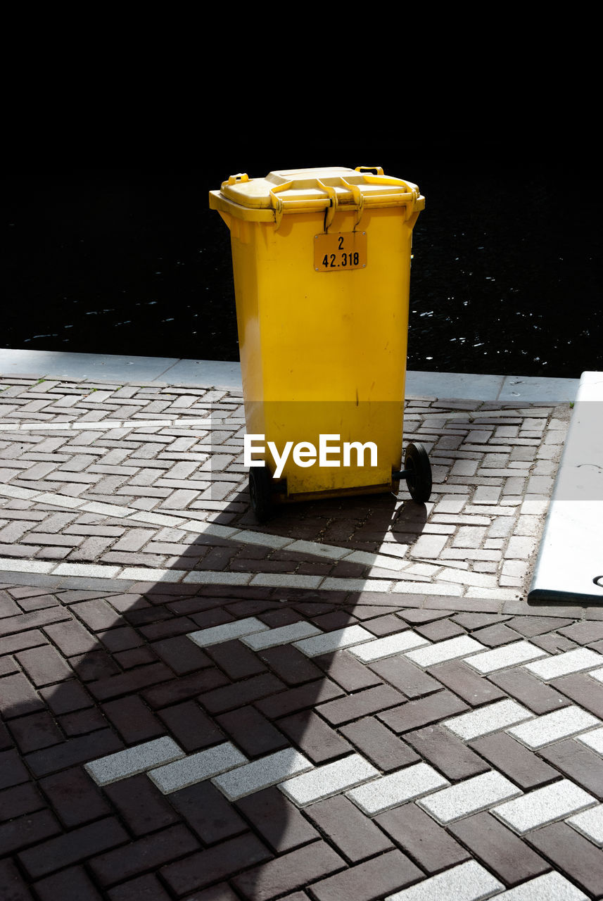 Yellow garbage can on footpath during sunny day