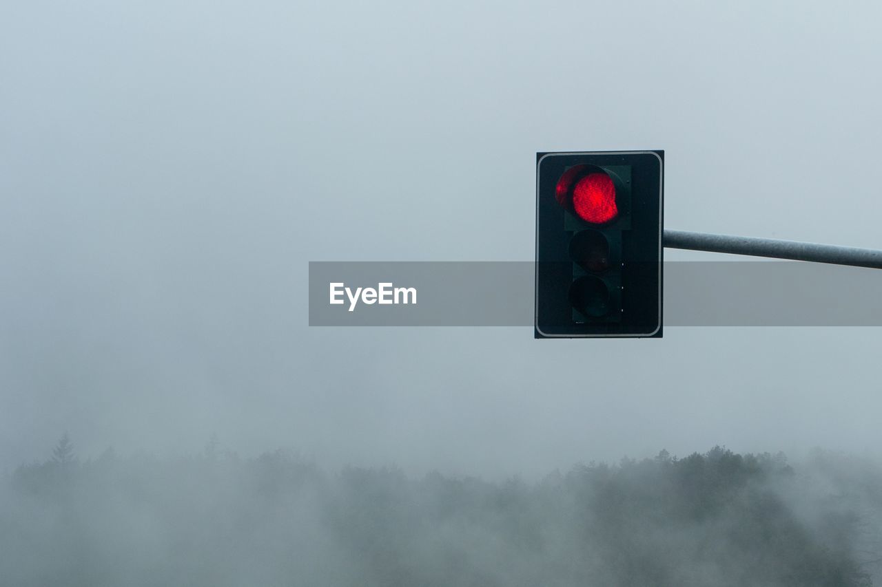 Illuminated road signal against sky during foggy weather