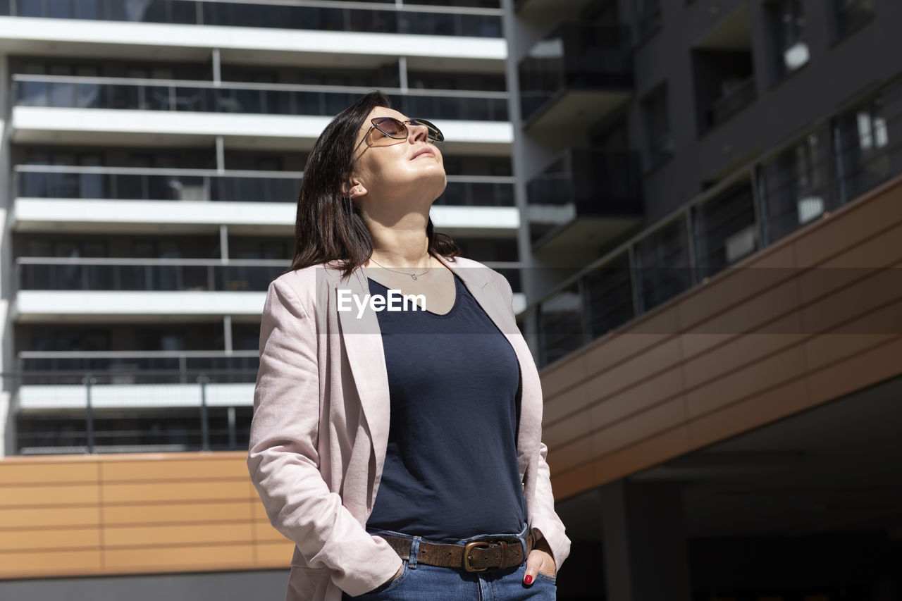 Happy mature 40 yo woman enjoys view of new apartment campus, complex in daytime. female brunette