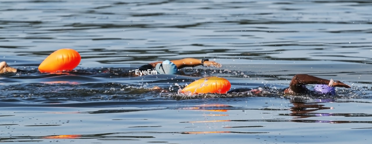 Two black triathletes are swimming together with orange safety buoys.