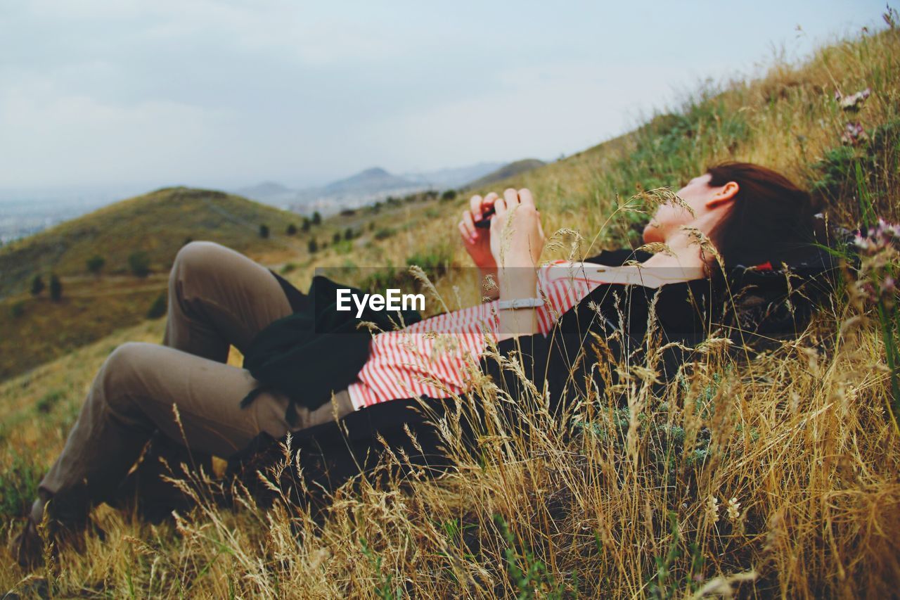 Young woman relaxing on grassy field against sky