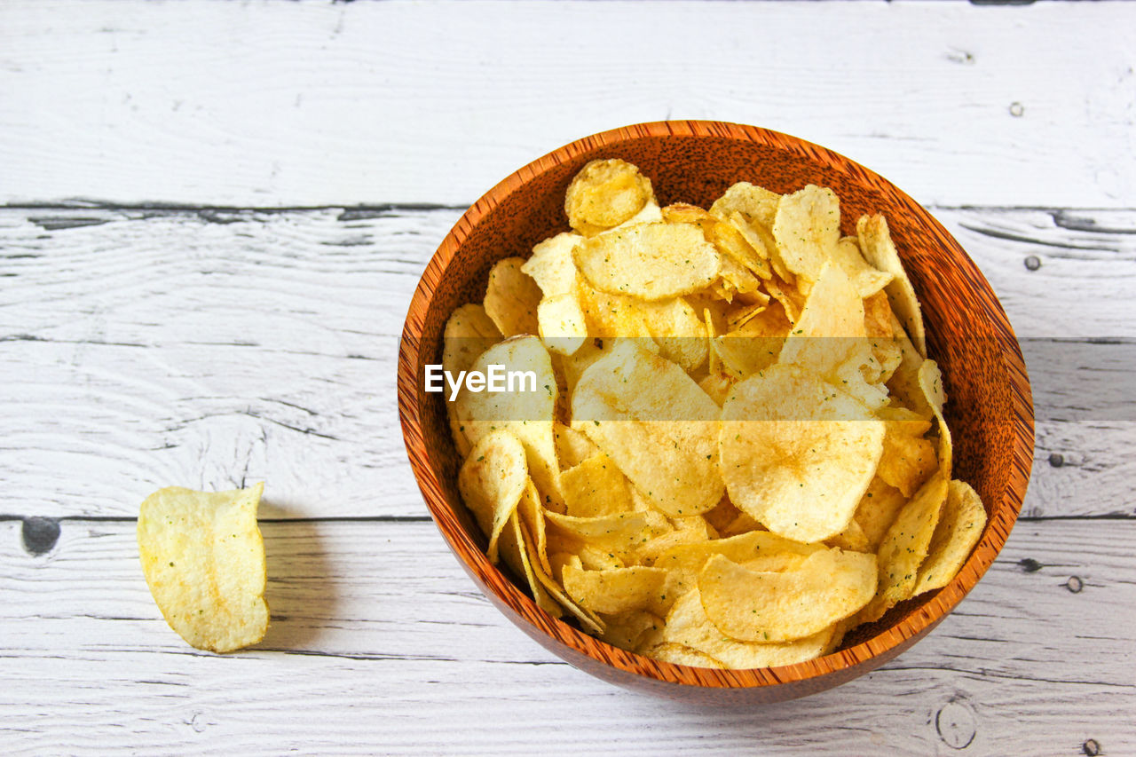 Potato chips or crisps in wooden bowl against white wooden background. pile of potato chips.