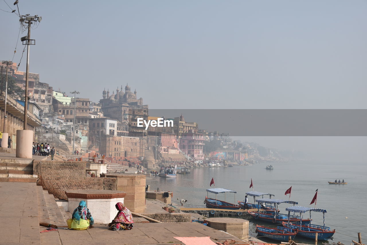 People on ganges by city against sky