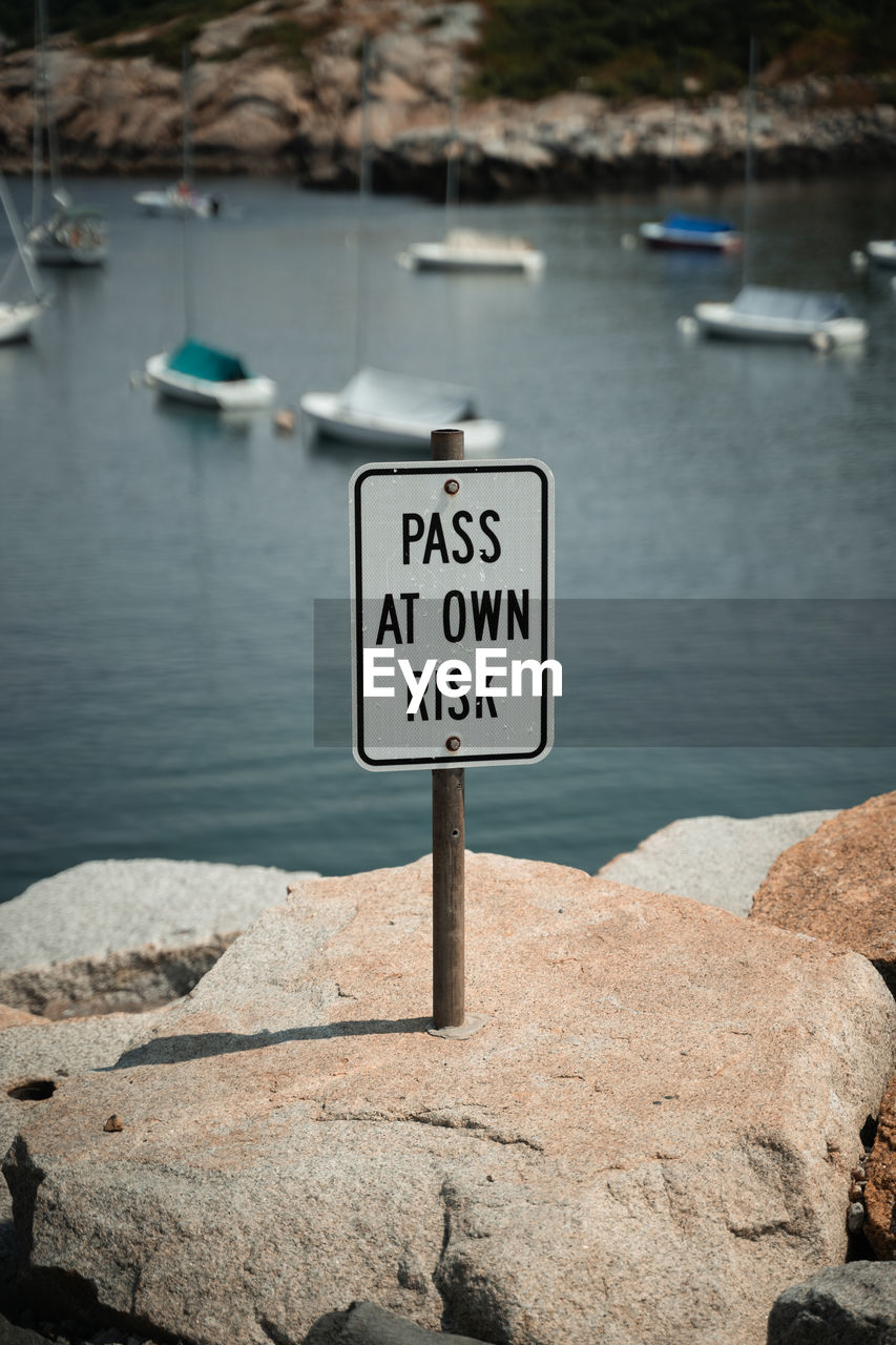 water, communication, sign, text, western script, nature, sea, no people, rock, day, information sign, guidance, transportation, nautical vessel, warning sign, outdoors, beach, harbor, focus on foreground, land, tranquility, road sign, mode of transportation, vehicle