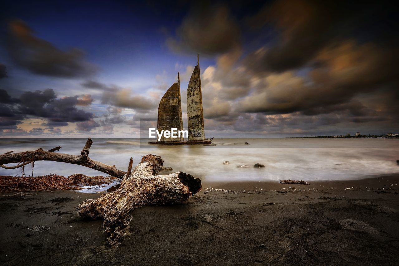 DRIFTWOOD ON BEACH BY SEA AGAINST SKY AT SUNSET