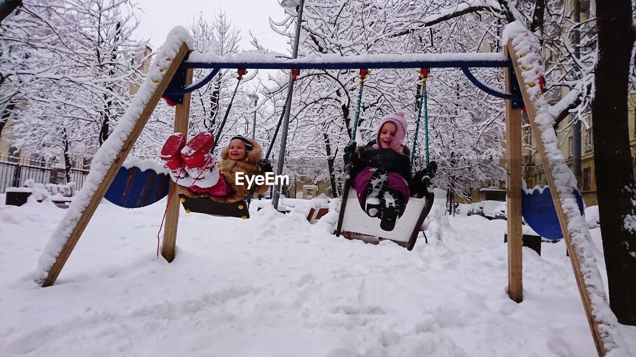 Kids on swing over snow covered field during winter