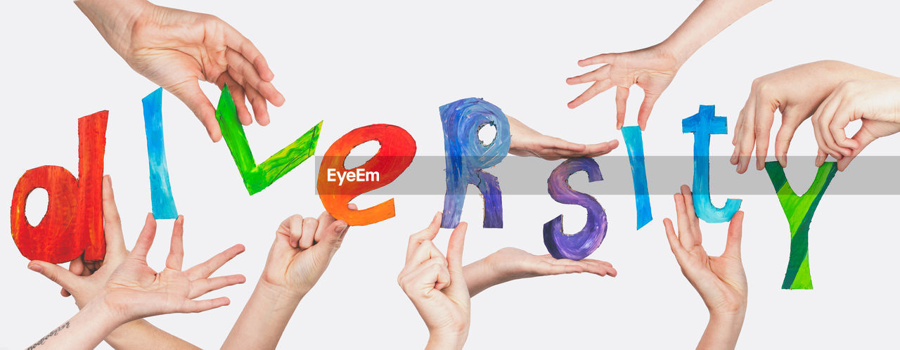 Cropped hands of people holding multi colored alphabets against white background