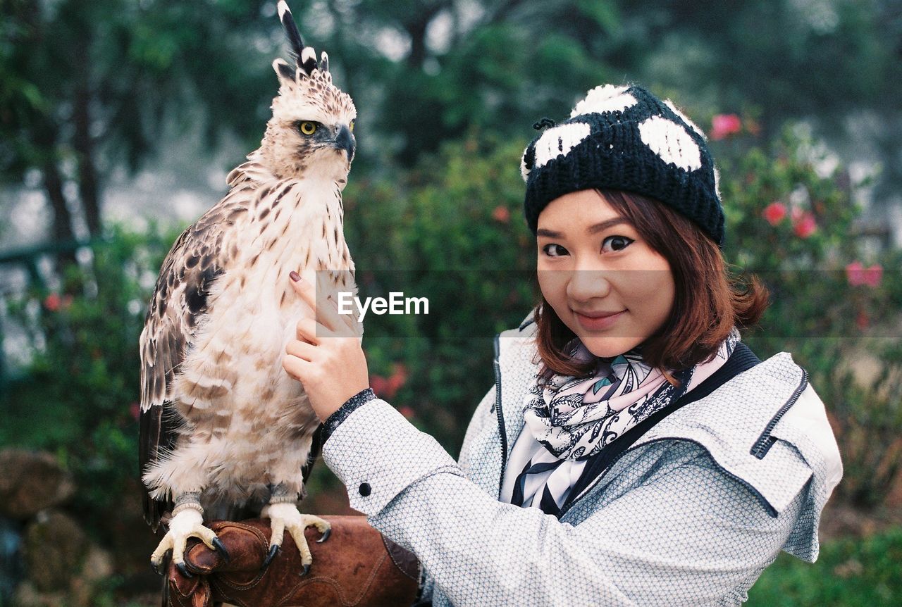 Portrait of woman standing by owl against trees