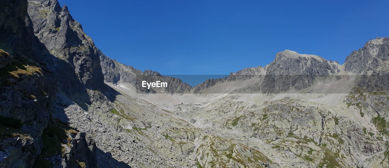 Panoramic view of rocky mountains against clear blue sky