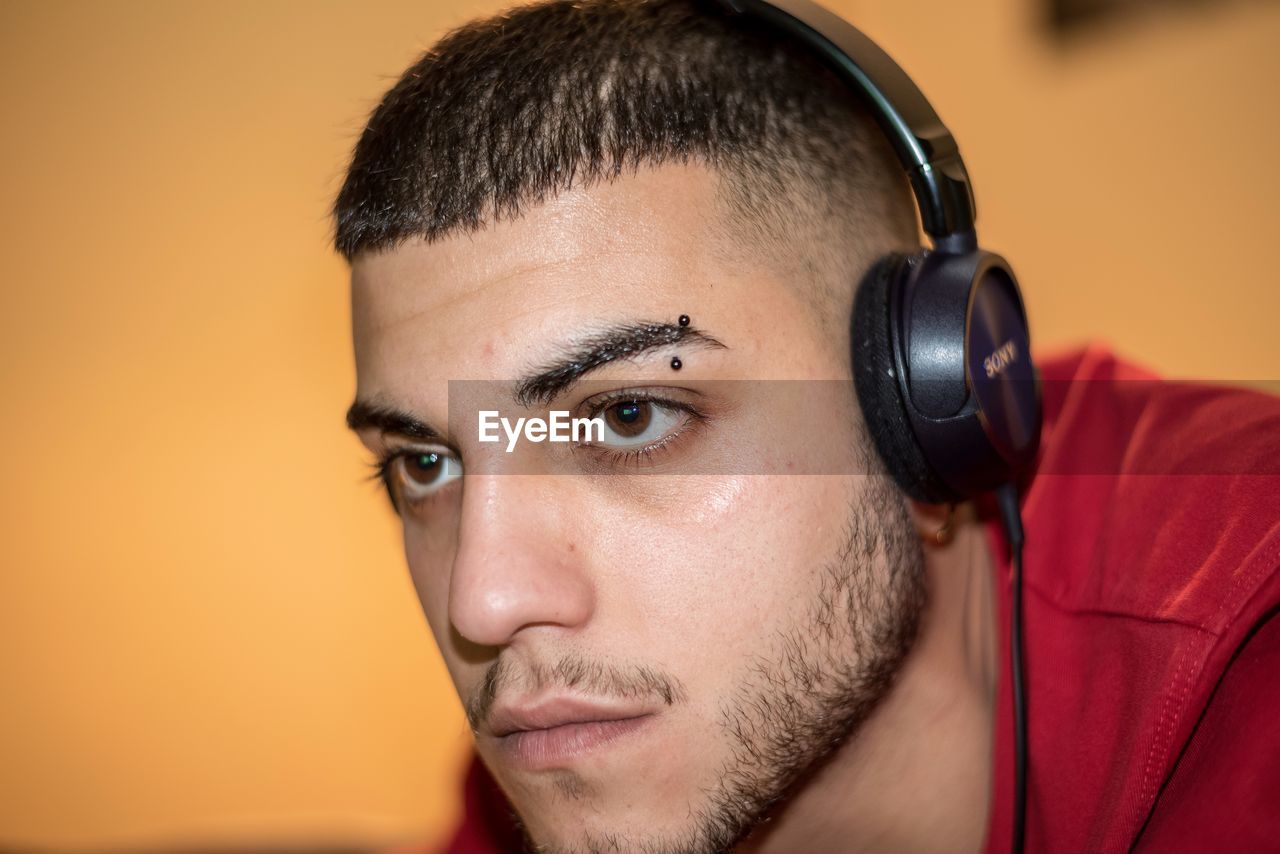 Close-up of young man listening music against orange background