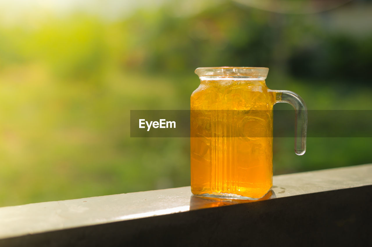 Close-up of orange juice in glass jar on railing