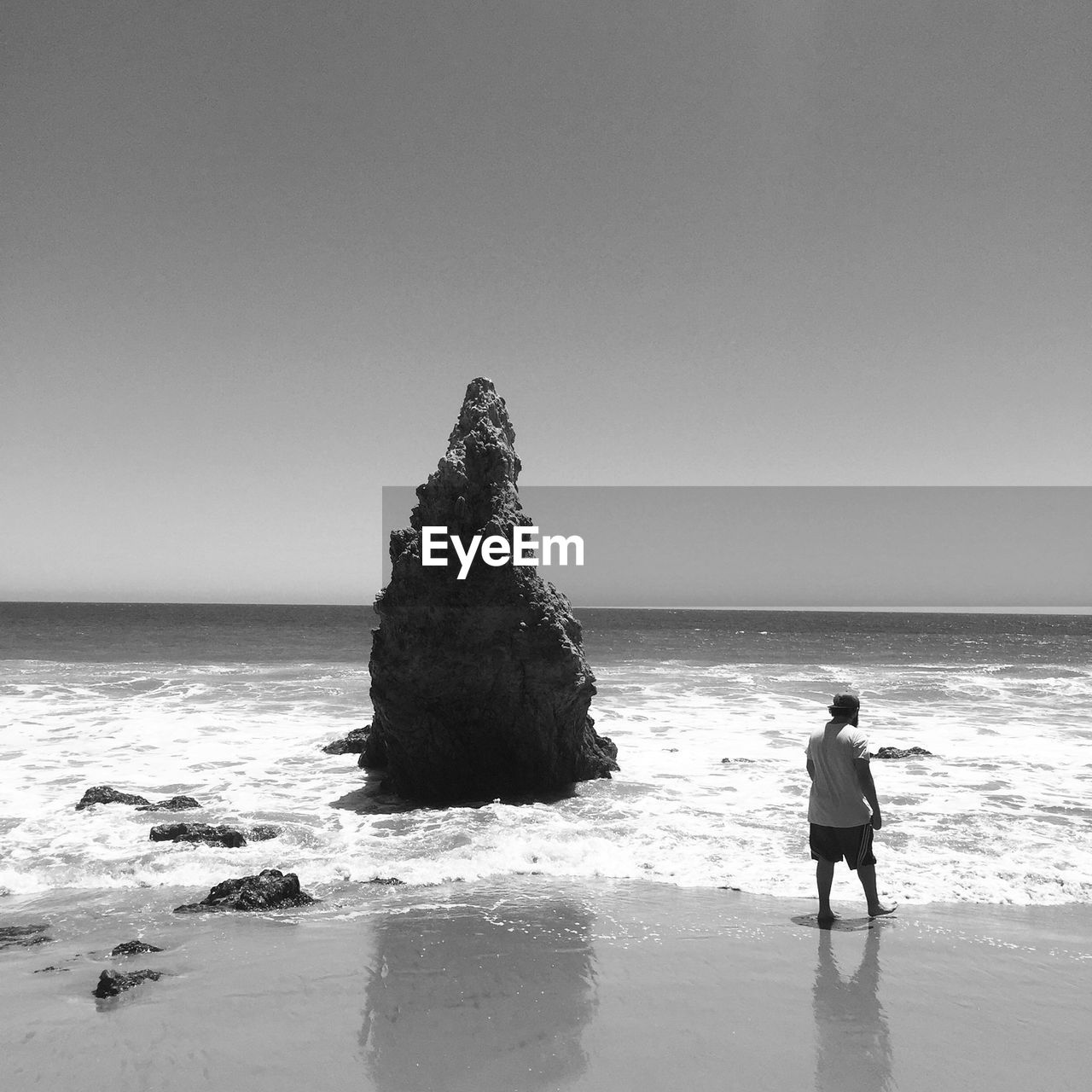 Rear view of man standing at beach against clear sky